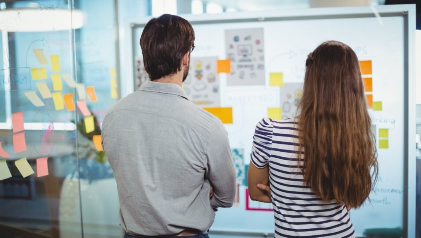Male and female executives looking at whiteboard in office