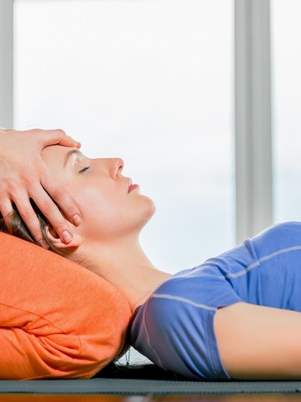 Close up portrait young beautiful girl making face head massage. Model lying on the knees of a masseuse in a yoga studio. Treatment, rest, relaxation, health skin care, spa